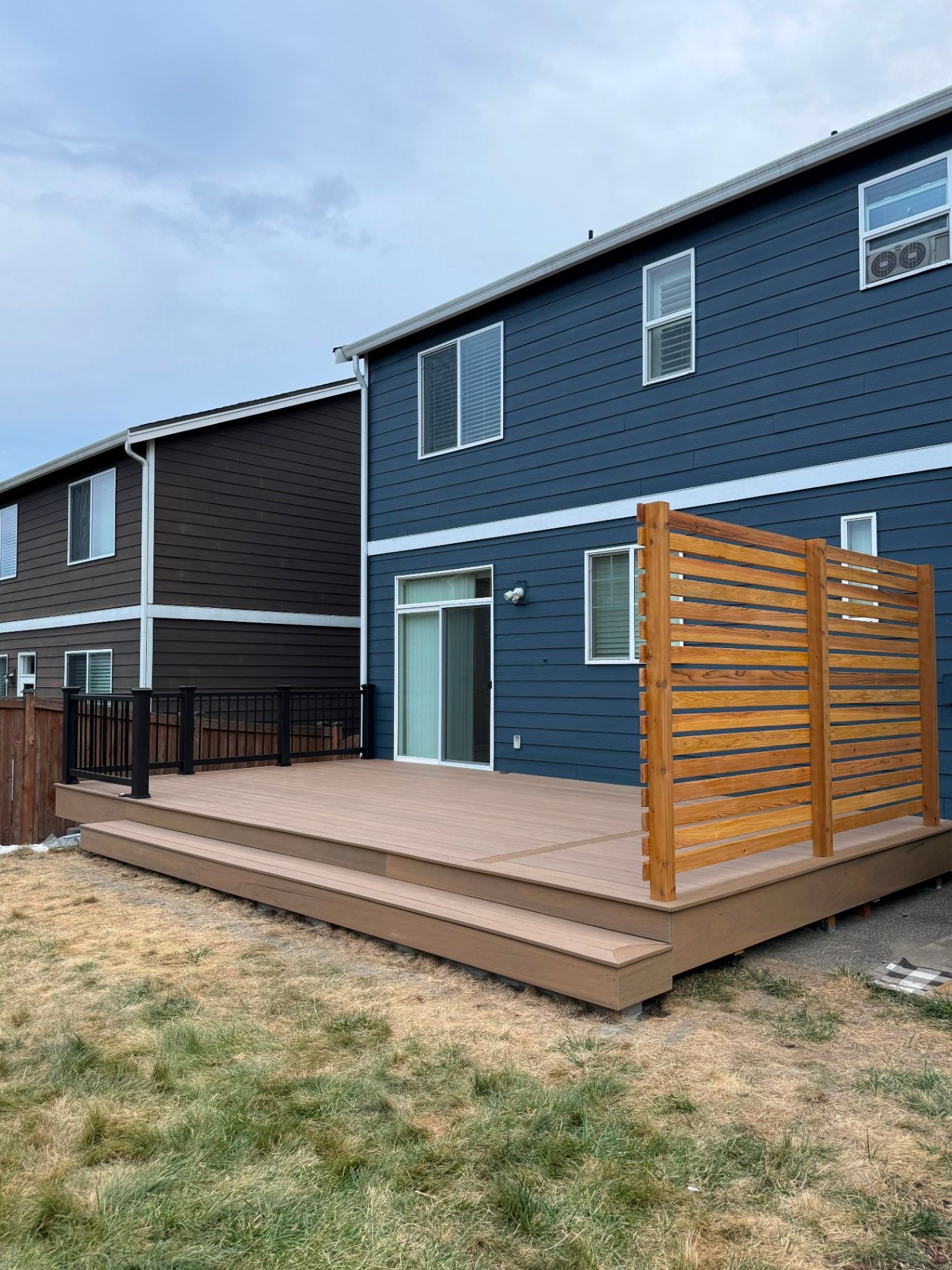 Finished low deck with a horizontal cedar privacy screen beside a dark blue home