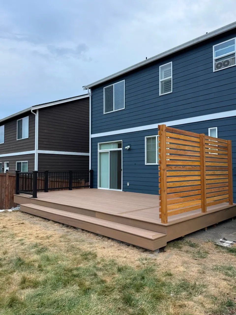 Finished low deck with black railings and a horizontal cedar privacy screen beside a dark blue home